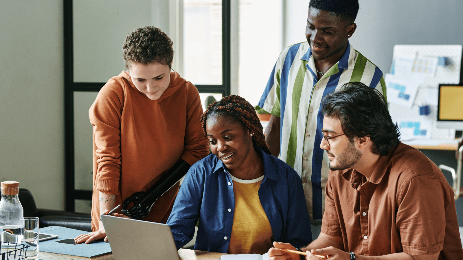 four young adults gathered around a laptop, collaborating