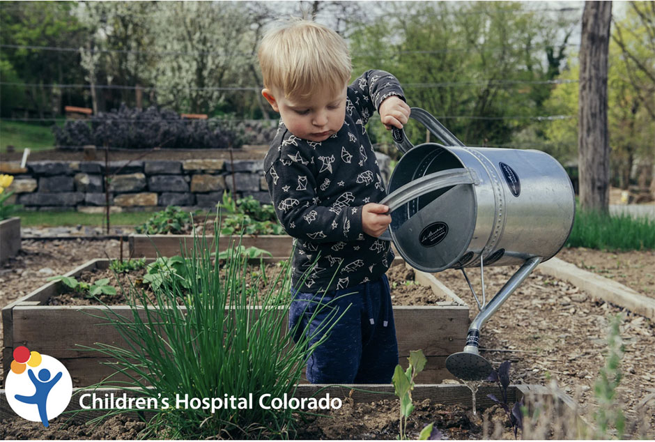 Little boy watering plants with a big watering can